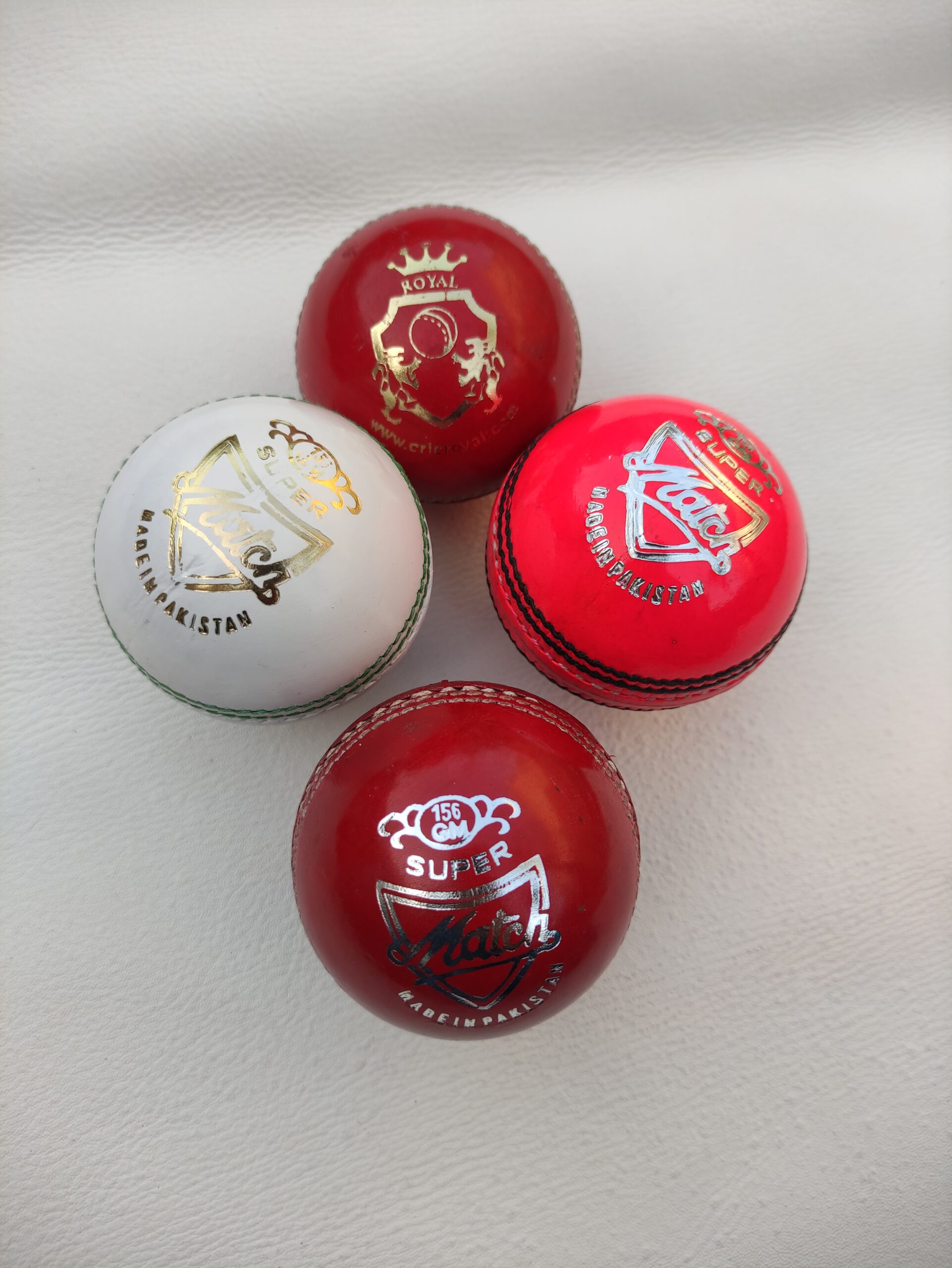 Four leather cricket balls in different colors placed together, each showing a unique view and logo design, highlighting the diverse color options and craftsmanship.