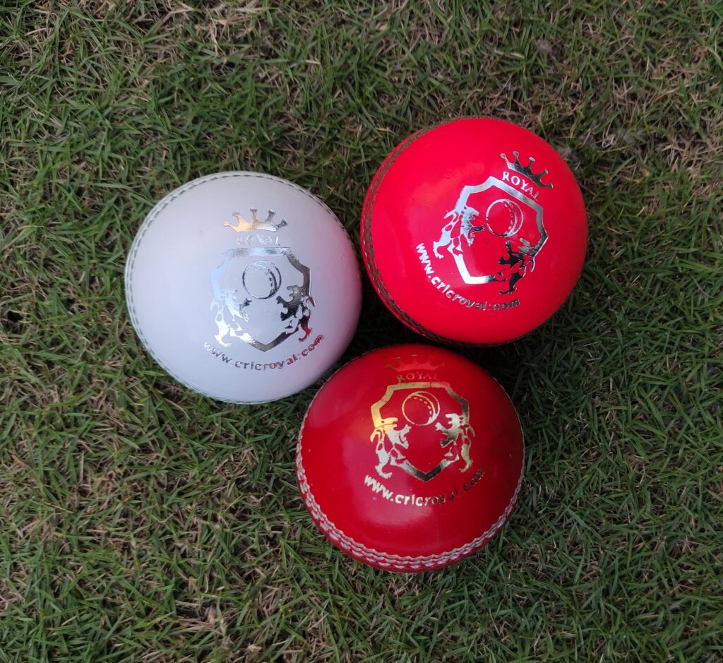 Three Kids Leather Cricket Hard Balls, each in a different color (red, white, and pink), placed on green grass in front-facing view, showcasing variety for junior training and play.