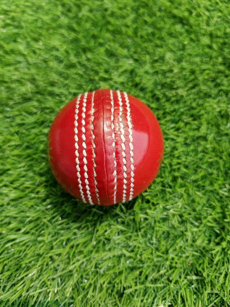 Red youth-size genuine leather junior cricket ball shown from side view with detailed stitching along the seam, designed for young players to practice with a durable and well-crafted ball