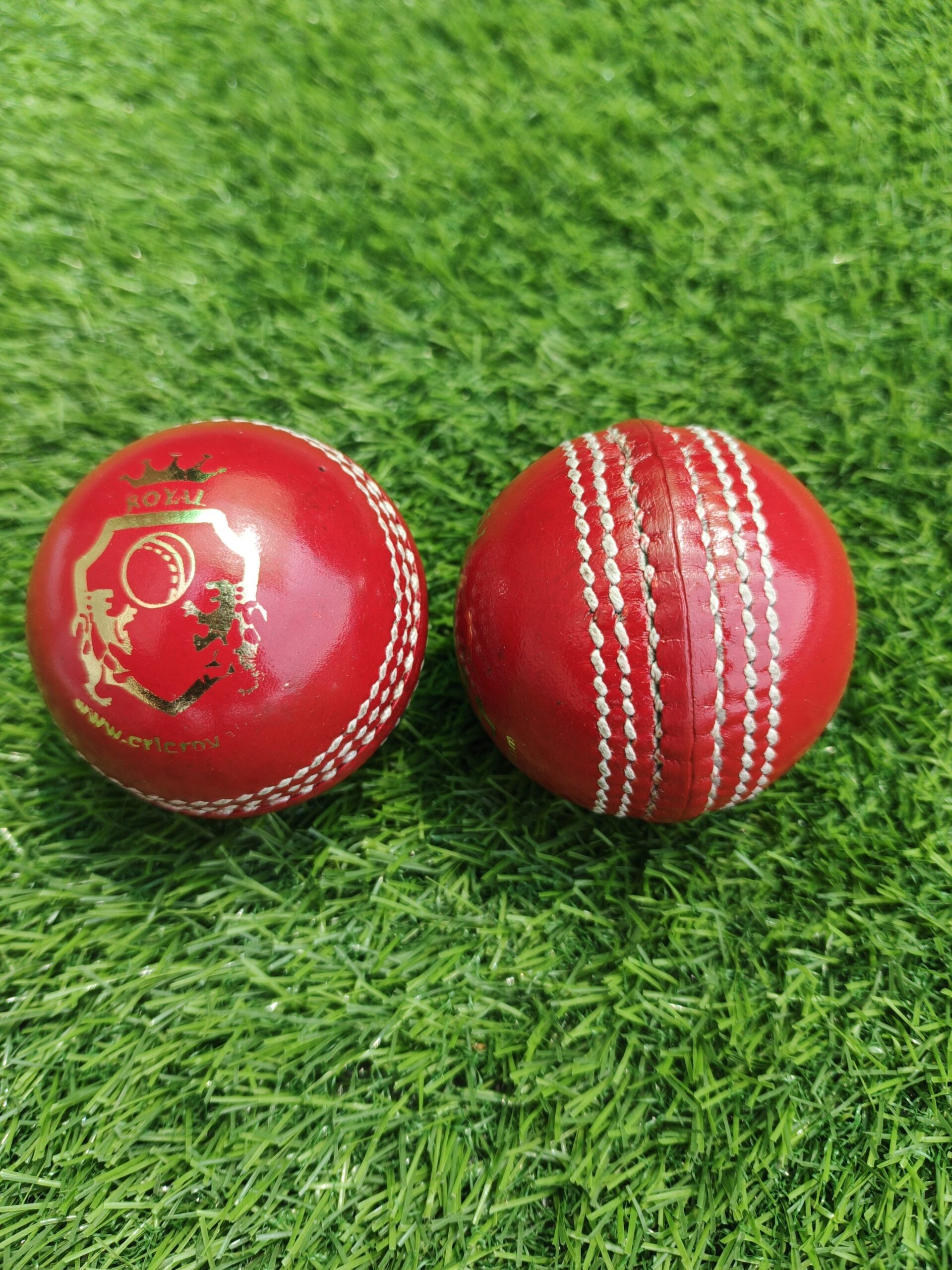Set of two youth-size genuine leather cricket balls in red color; one displayed from the front view showing the Royal Cricket logo, and the other from the side view highlighting the stitched seam, ideal for junior-level training and practice