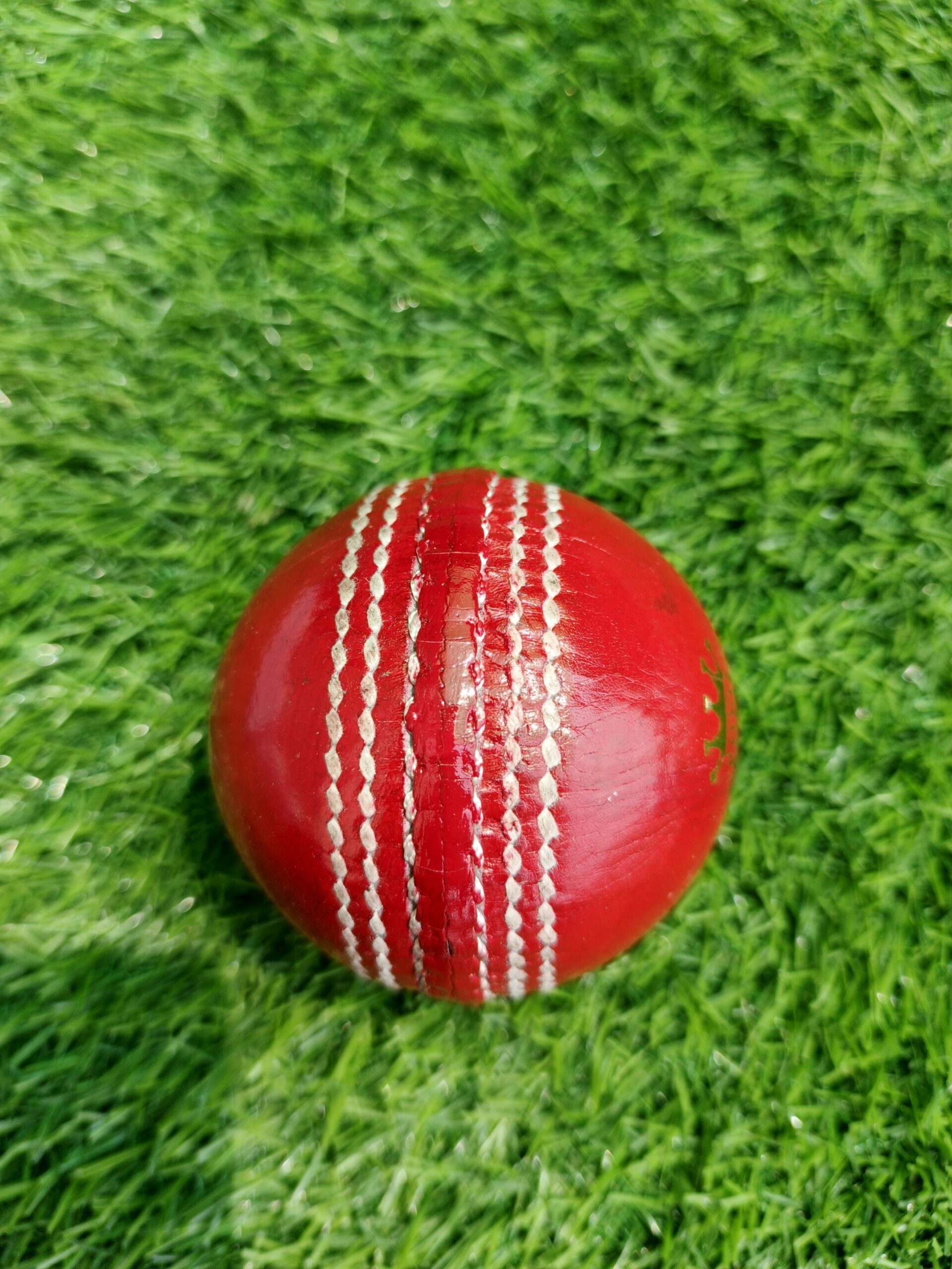 Red women-size genuine leather 4-piece cricket ball shown from side view, highlighting the tightly stitched seam and high-quality leather finish for professional-level women's cricket matches
