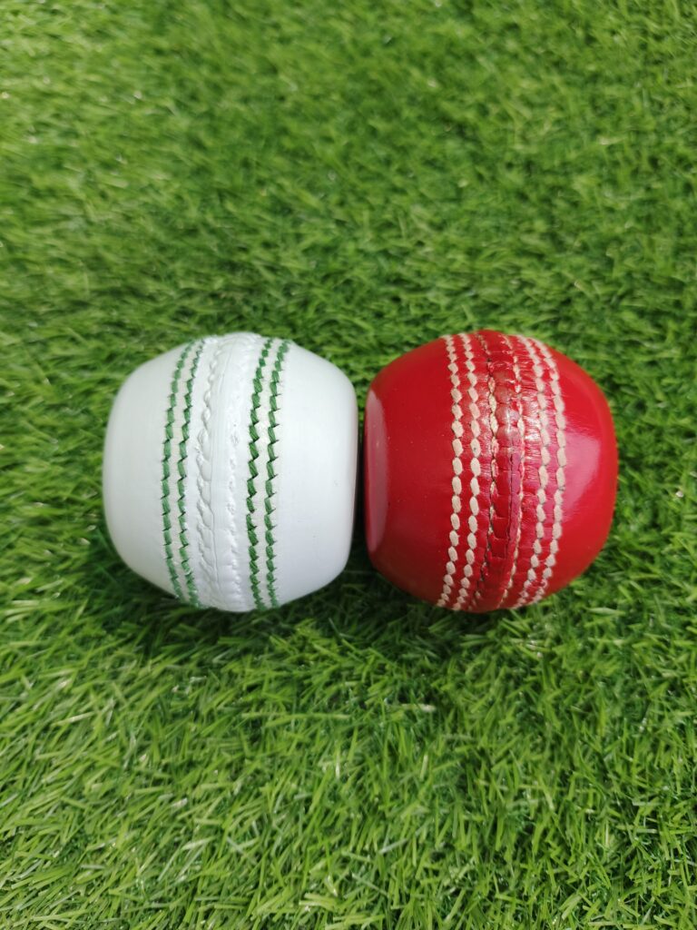 Side view of two flat seam cricket balls, one red and one white, designed for coaching and training, showcasing the stitched seam with a flat surface ideal for bowling practice