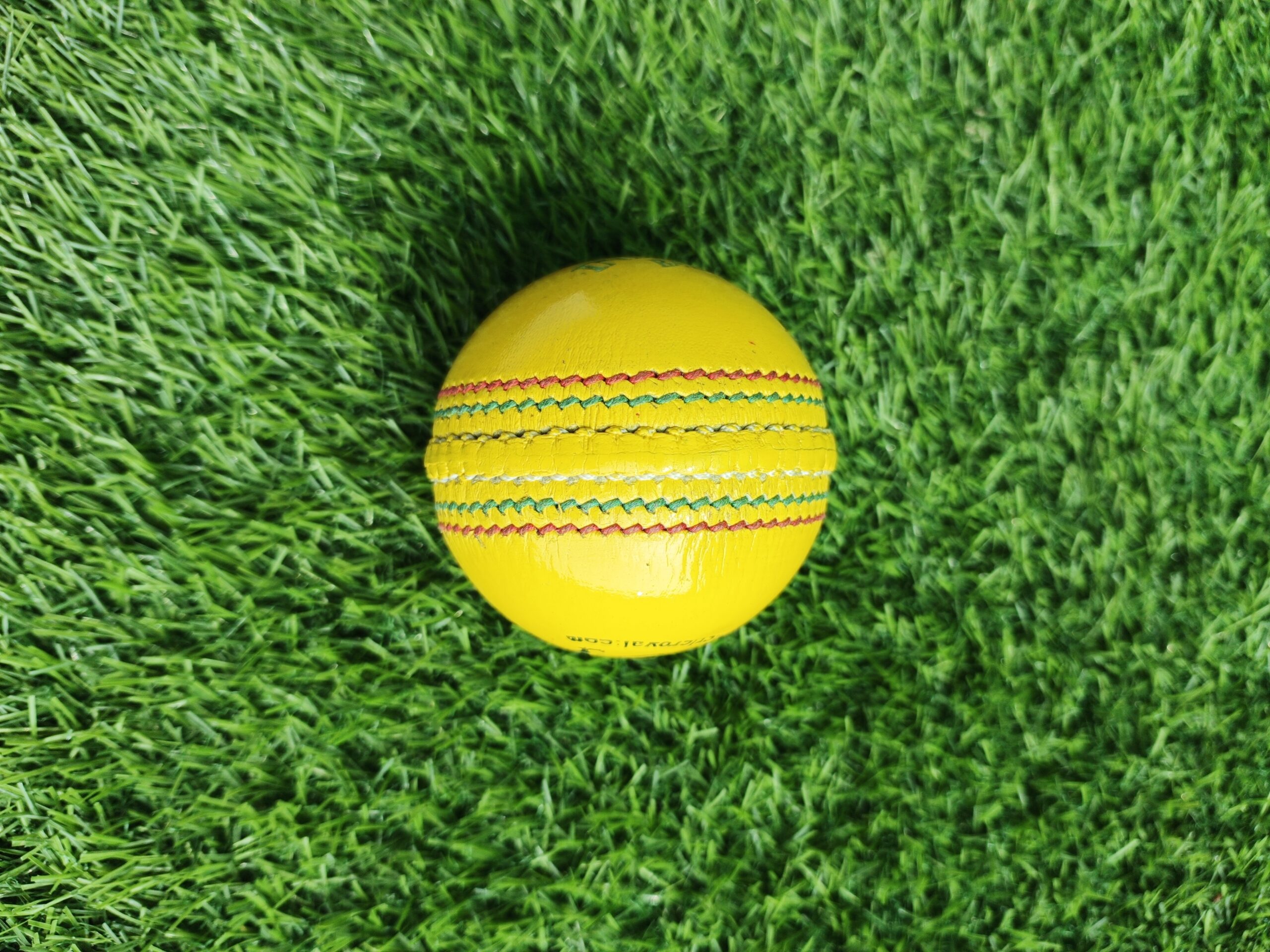 Yellow Indoor Premium Leather Cricket Ball shown from side view with full tight stitching visible across the seam, crafted for durable indoor use with premium quality finish