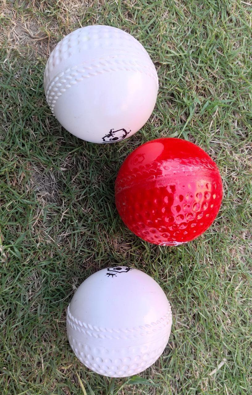 Set of three Swing Technique Molded Synthetic Cricket Hard Balls lying on grass; includes two white and one red ball, placed naturally to display durable synthetic build and aerodynamic swing design