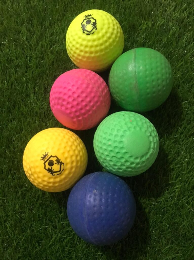 Six heavy-weight synthetic dimple balls lying on grass in different angles, ideal for training and practice sessions.