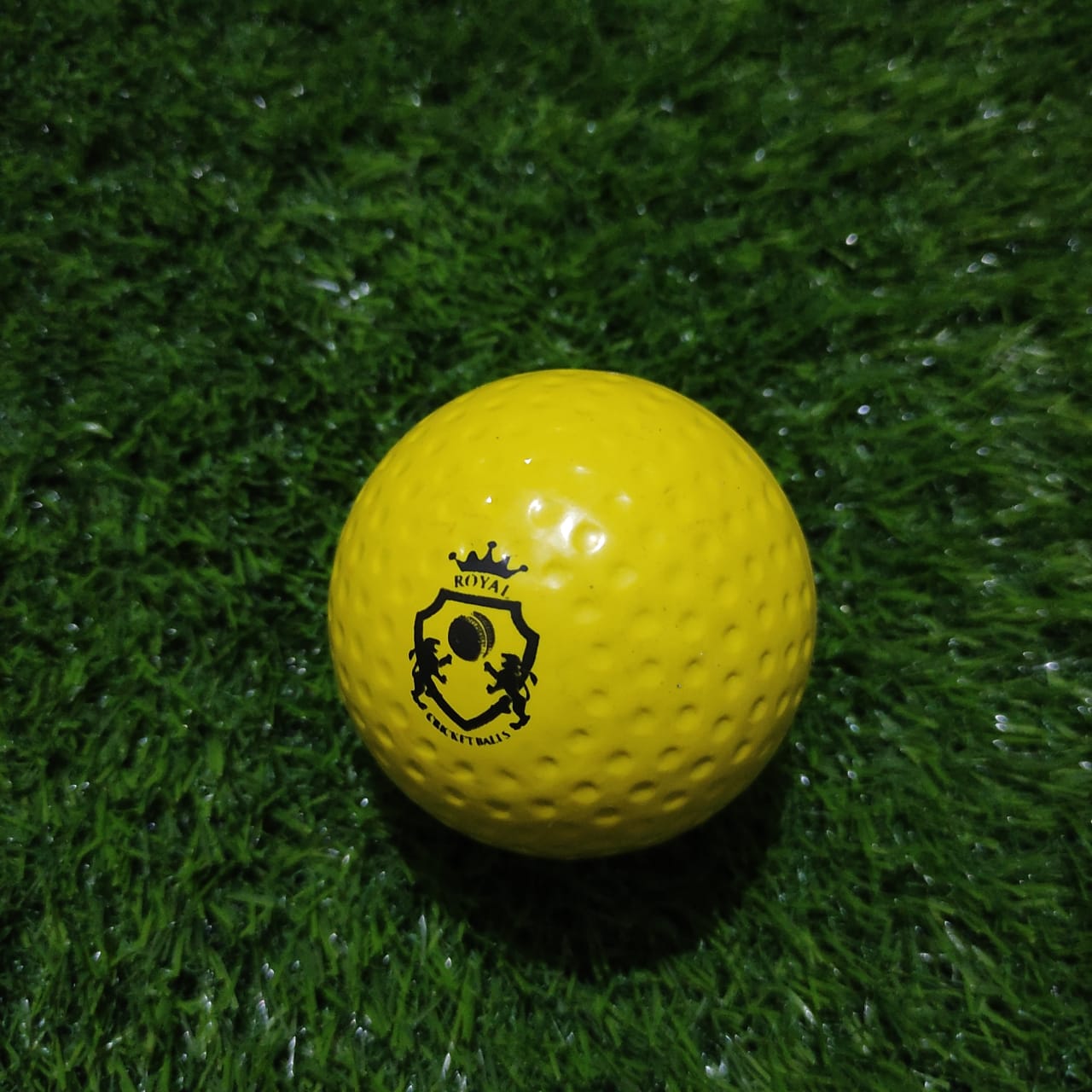 A front-facing yellow Dimple Soft Molded Synthetic Cricket Ball featuring a visible company logo, designed with waterproof material for consistent play in all weather conditions.