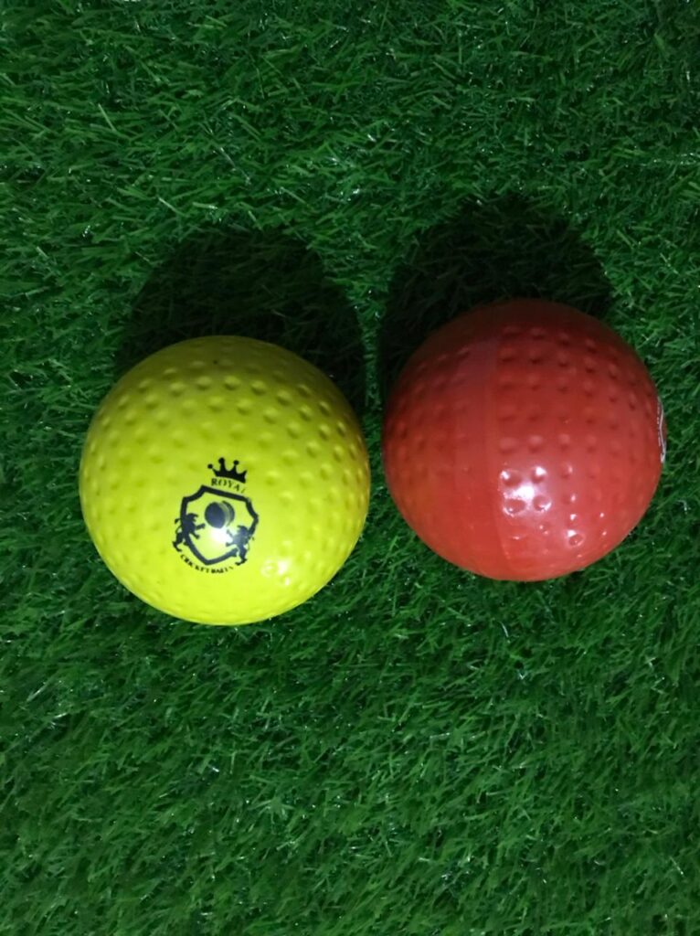 Set of two Wind Balls also known as Air or Hollow Soft Cricket Practice Balls; red ball shown from front with Royal Cricket logo, yellow ball placed sideways to show shape and detailing