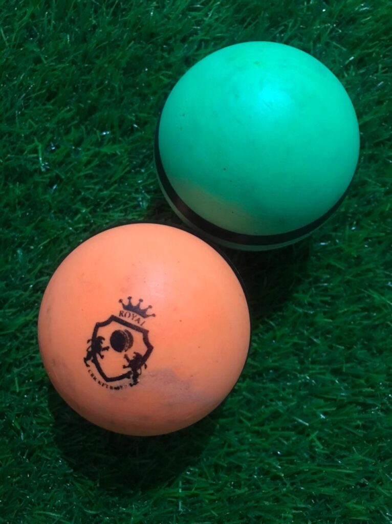 Two plain bowling machine balls placed at different angles, one in sky blue and the other in orange, highlighting smooth surface and build quality