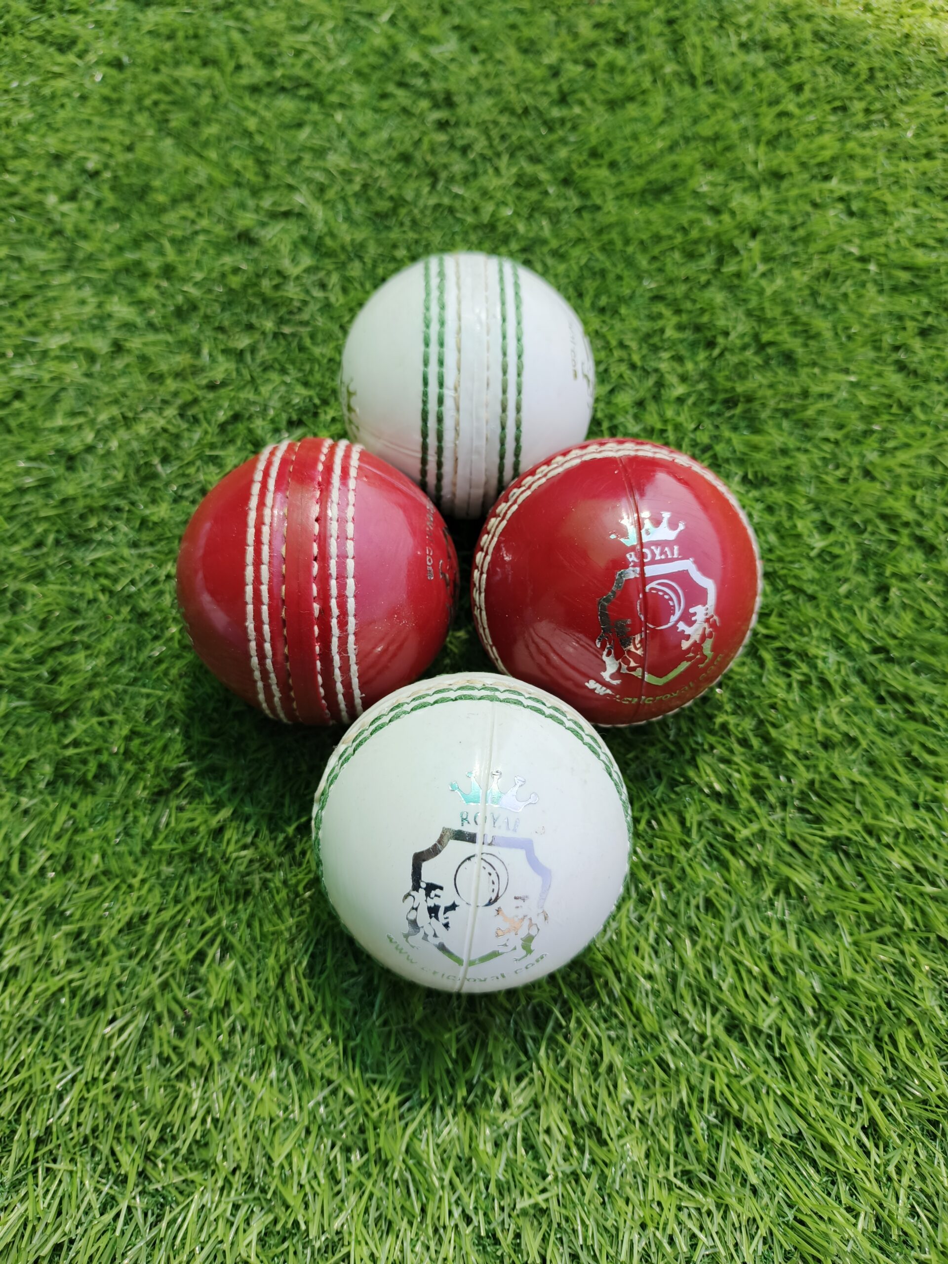 Set of four PVC Practice Cricket Hard Balls in red and white colors lying on grass, with a mix of front and side views showing stitched seams and detailed surface, perfect for professional training sessions