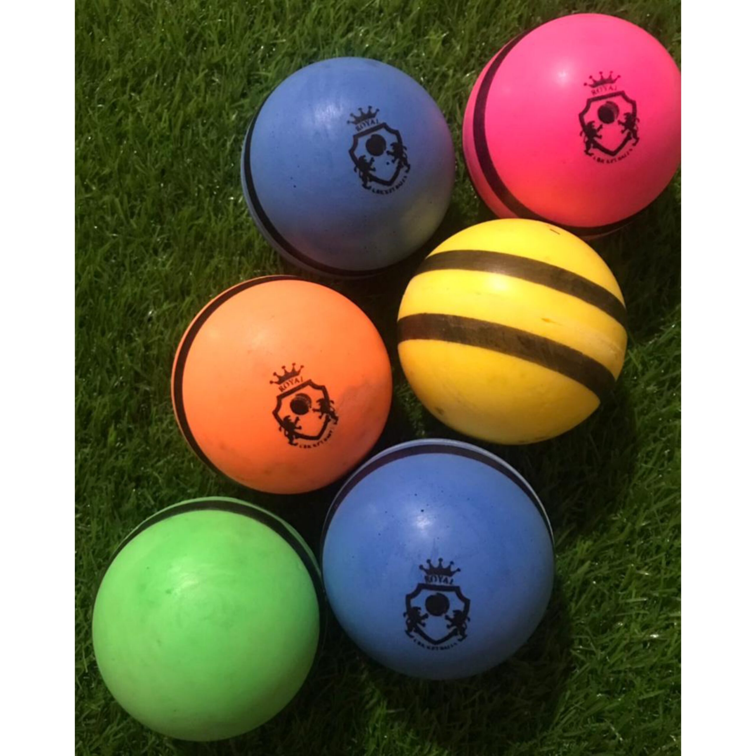 Set of 6 plain bowling machine balls in various colors placed on grass surface, each positioned differently to show angles and vibrant design
