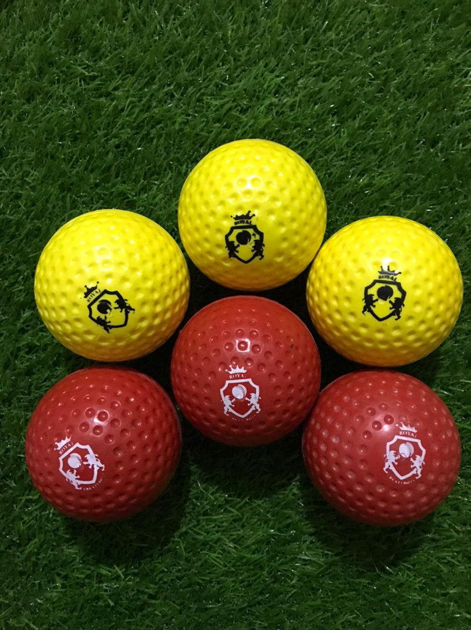 Six dimple bowling machine balls in red and yellow colors lying on a grass surface, showcasing machine-ready texture with dimples from various angles